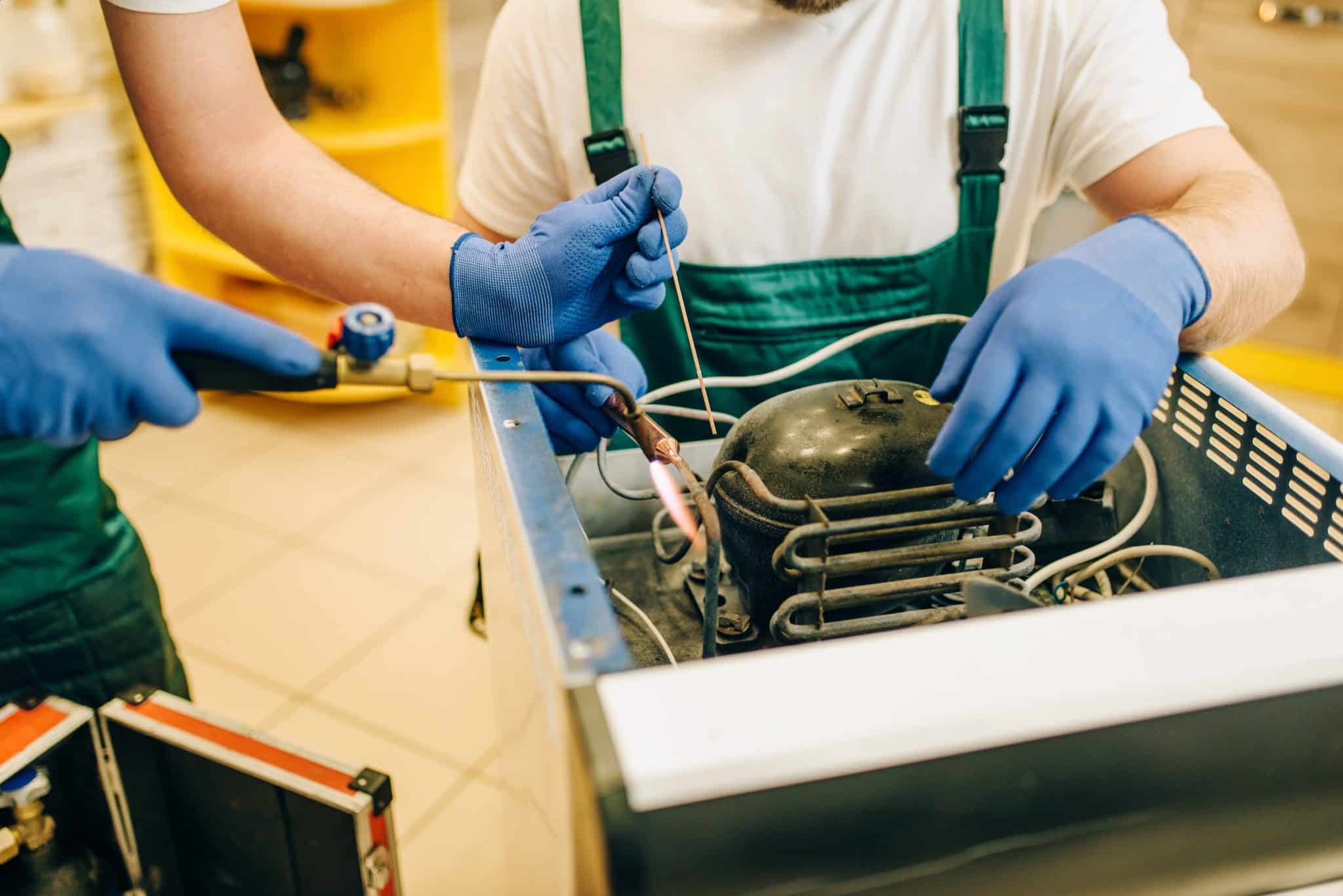 Appliance repairmen with burner repairs refrigerator at home